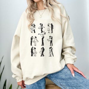 Puede incluir: Una sudadera de color crema con un estampado gr&aacute;fico de nueve siluetas negras de parejas bailando.