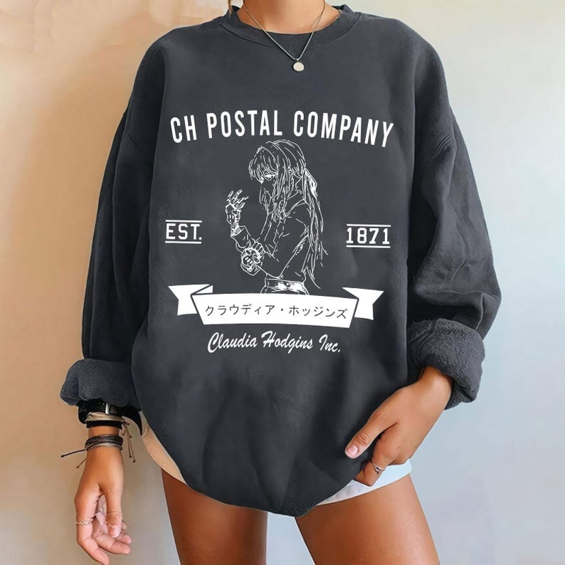 May include: Dark gray sweatshirt with white graphic text and illustration. The text reads "CH POSTAL COMPANY" above an illustration of a person. Below the illustration is a banner with Japanese text and the name "Claudia Hodgins Inc." The sweatshirt also has the text "EST. 1871".