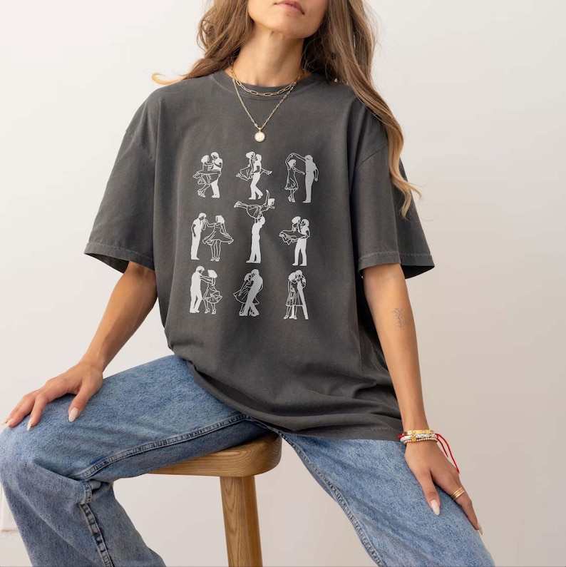 Puede incluir: Una camiseta gris de gran tama&ntilde;o con un gr&aacute;fico blanco de parejas bailando. La camiseta la lleva puesta una persona con el pelo largo y casta&ntilde;o y se combina con unos vaqueros azules.