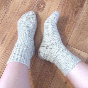 Peut inclure: Une paire de chaussettes en crochet beige sur un sol en bois.