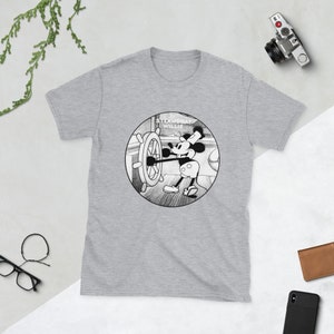 May include: A gray t-shirt with a black and white illustration of Mickey Mouse as Steamboat Willie. The illustration shows Mickey Mouse steering a ship's wheel.
