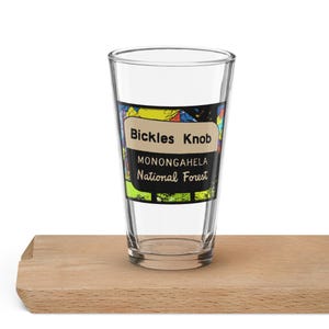 May include: A clear glass pint glass with a colorful graphic of a map and the text "Bickles Knob Monongahela National Forest".