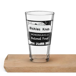 May include: A clear glass pint glass with a black and white image of a sign that reads "Bickles Knob Monongahela National Forest".