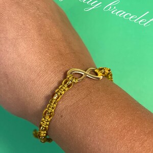 May include: A gold infinity symbol charm bracelet with a gold cord and small gold beads. The bracelet is on a person's wrist.