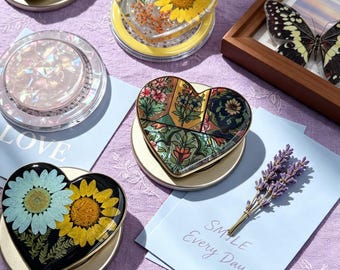May include: A collection of heart-shaped resin coasters featuring various designs including pressed yellow sunflowers, green foliage, intricate floral patterns in green and gold, and a combination of a light blue daisy and a yellow sunflower.