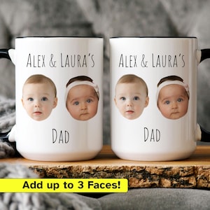 May include: Two white ceramic mugs with black handles and rims. Each mug features a baby's face, the text "ALEX & LAURA'S" above, and "DAD" below. The mugs have a personalized design. The bottom of the image has the text "Add up to 3 Faces!"