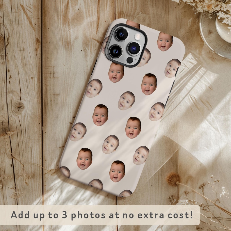 May include: A white iPhone case with a repeating pattern of baby faces. The case has a camera lens cutout and a black border.