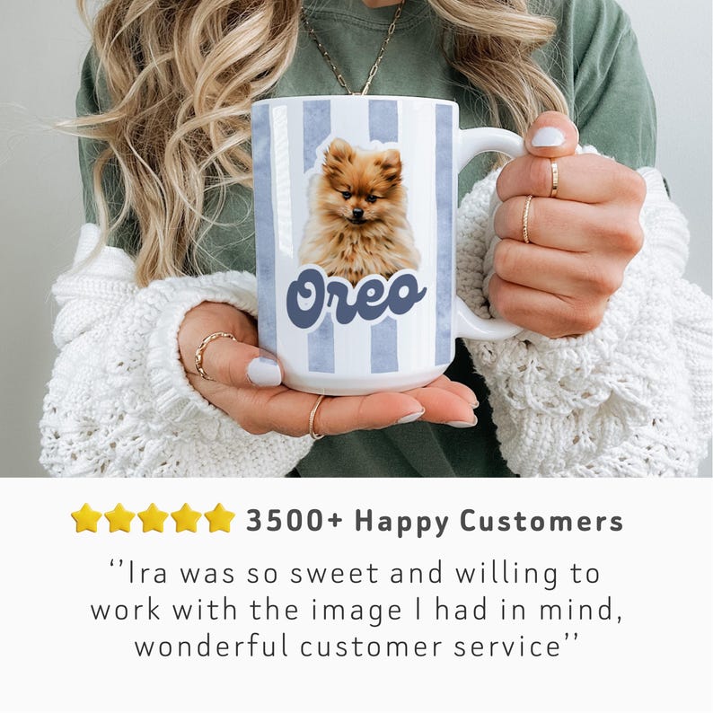 May include: White ceramic mug with blue vertical stripes and a Pomeranian dog illustration. The dog's name, "Oreo," is written in blue script. The mug is held by a person wearing a white sweater. The mug is a great gift for dog lovers.