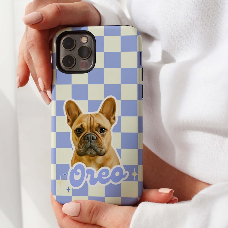 K&ouml;nnte beinhalten: Eine Handyh&uuml;lle mit einem hellbraunen Franz&ouml;sischen Bulldoggen und dem Namen "Oreo". Die H&uuml;lle hat ein blaues und cremefarbenes Schachbrettmuster. Die Handyh&uuml;lle wird von einer Person gehalten.