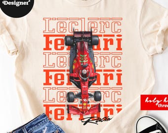 以下が含まれることがあります： クリーム色のTシャツで、上から見た赤いF1レースカーのグラフィックが中央に配置され、その下に「Leclerc」と「Ferrari」という赤い文字が繰り返されています。Tシャツは青いデニムのショートパンツと黒と白のハイカットスニーカーと組み合わされています。