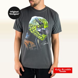 Puede incluir: Camiseta gris oscuro con una imagen de un casco de carreras en verde ne&oacute;n y negro. La camiseta incluye el texto "Original Designer" y "holy hustle threads".