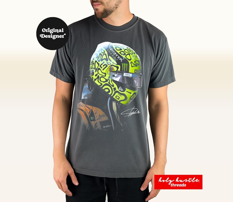 Puede incluir: Camiseta gris oscuro con una imagen de un casco de carreras en verde ne&oacute;n y negro. La camiseta incluye el texto "Original Designer" y "holy hustle threads".