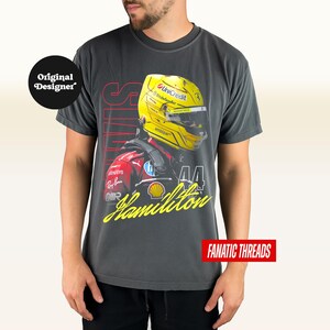 May include: Dark grey t-shirt with a graphic of a Formula 1 driver wearing a yellow helmet. The design includes the name "Hamilton" in yellow script, the number "44", and the word "SPEED" in red. The shirt has the text "FANATIC THREADS".