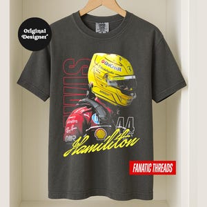 May include: Charcoal grey t-shirt with a graphic of a Formula 1 driver in a yellow helmet. The shirt displays the name "Hamilton" in yellow script, the number "44", and the text "FANATIC THREADS".