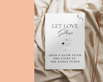 May include: A white card with black text that reads "Let Love Glow" with a small illustration of stars. The text below reads "Grab a glow stick and light up the dance floor".