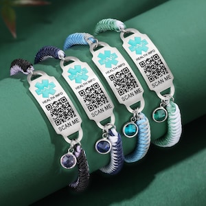 May include: Four medical alert bracelets with woven bands in various colors: black, navy, blue, and green. Each bracelet features a silver tag with a medical symbol, the words "HEALTH INFO" and "SCAN ME", and a QR code. Each bracelet has a charm.