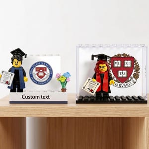 May include: Two Lego figures in graduation attire, one with a Phillips Exeter Academy logo and the other with a Harvard University logo. Each figure holds a diploma. The Phillips Exeter figure has a blue and black robe, and the Harvard figure has a red and black robe.
