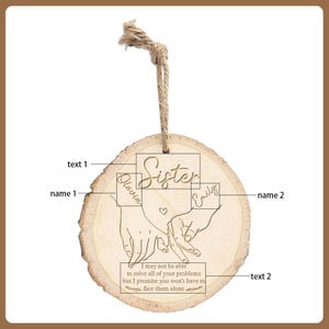 May include: A wooden ornament with a natural wood grain finish. The ornament features the word "Sister" and the names "Olivia" and "Emily" engraved on it. Below the names, there is an engraved image of two hands holding each other. The text "I may not be able to solve all of your problems but I promise you won't have to face them alone" is also engraved.