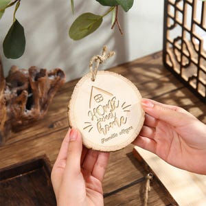 May include: A round, wooden ornament with the phrase "Home sweet home" engraved in a script font, along with a small house illustration. The ornament has a natural wood grain and a twine loop for hanging. The text "Familie Meyer" is also engraved.