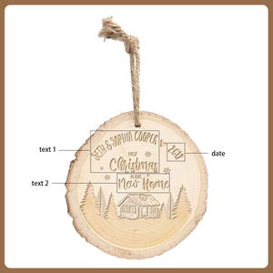 May include: A round, wooden Christmas ornament with a natural wood grain finish. The ornament features engraved text: "Seth & Sophia Cooper," "First Christmas," and "Now Home," along with the year "2019." A cabin and trees are also engraved.