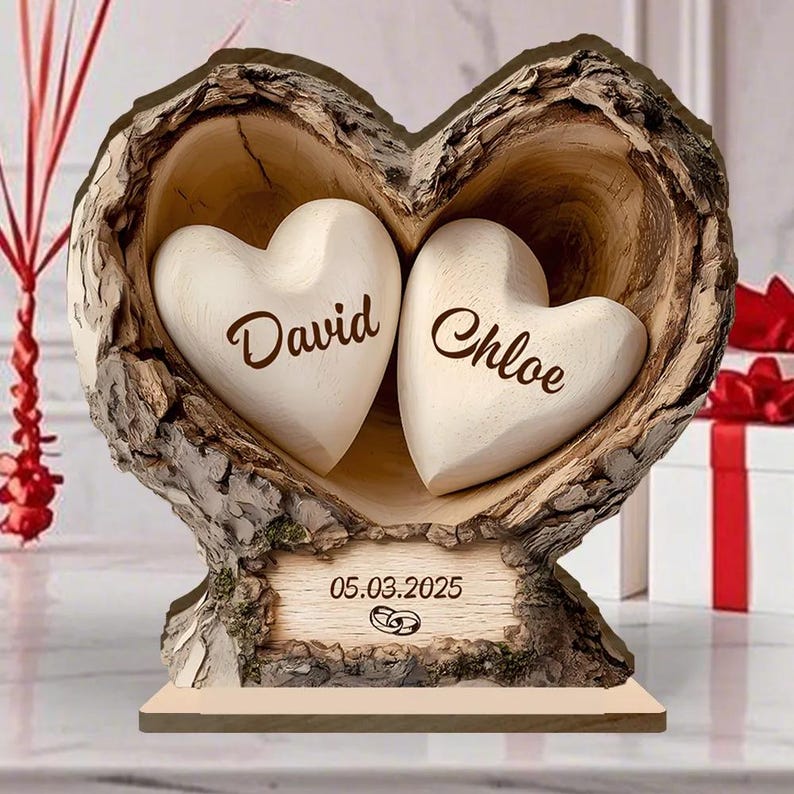May include: A wooden heart-shaped sculpture with two white heart-shaped inserts, each bearing a name. The sculpture has a rustic bark-like exterior and a wooden base. The date 05.03.2025 and wedding rings are engraved on a wooden plaque.