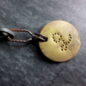 May include: A gray metal key attached to a circular brass-toned tag by a dark, textured metal link. The round tag features a small, dotted letter y embossed on its surface. The key has a simple, utilitarian design with a rounded head.