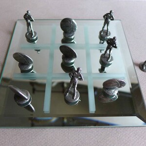 May include: A silver tic-tac-toe game set on a mirrored surface. The game pieces are silver figurines of basketball players and silver discs.