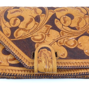 May include: A brown leather satchel with a flap closure and a decorative floral design. The bag has a long strap and is made of genuine leather.