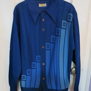 May include: A long-sleeve button-up shirt in royal blue featuring a pointed collar and a front graphic pattern of vertical bars and squares in varying shades of light and medium blue. The shirt has a row of brown buttons down the center front.