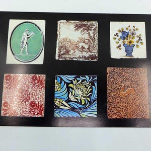 May include: A black display board featuring six decorative tiles with various designs. The tiles include a classical figure in an oval, a lion scene, a floral arrangement, a red floral pattern, a blue and yellow floral design, and a brown deer scene.