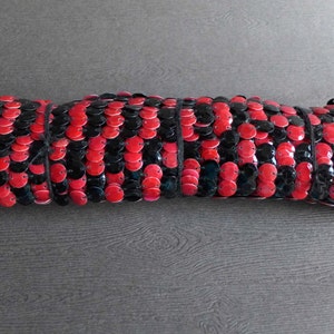 May include: A close-up of a red and black sequined trim. The trim is made of small, round sequins that are sewn together in a repeating pattern.