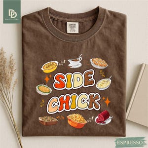 May include: Espresso-colored t-shirt with the words "SIDE CHICK" in a retro font, surrounded by illustrations of various side dishes. The shirt has a crew neck and a Comfort Colors tag.