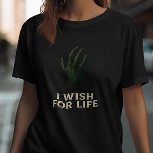 May include: Black t-shirt featuring a green, clawed hand graphic. The text "I WISH FOR LIFE" is printed below the hand in a serif font. The shirt is made of a soft material.