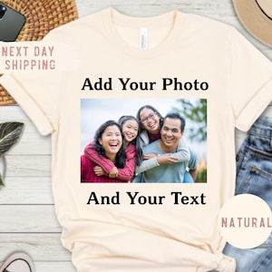 May include: A cream-coloured t-shirt featuring a family photo and the text "Add Your Photo And Your Text." The shirt is styled with blue jeans, a straw hat, sunglasses, and black trainers. A small potted plant and a phone are also visible.
