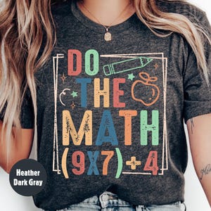 May include: Heather dark gray t-shirt with the text "DO THE MATH (9x7)+4" in colorful block letters. The design includes a pencil, apple, and stars. The shirt is a casual style.