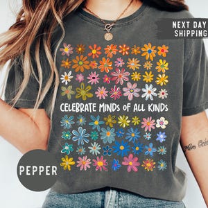 May include: A charcoal grey t-shirt with a colorful floral design and the text "Celebrate Minds of All Kinds".