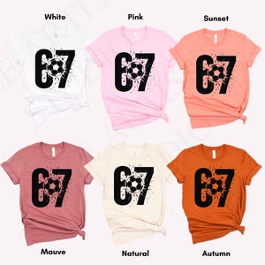 May include: Six short-sleeved t-shirts in white, pink, sunset, mauve, natural, and autumn colors. Each shirt features the number "67" with a soccer ball graphic in black.