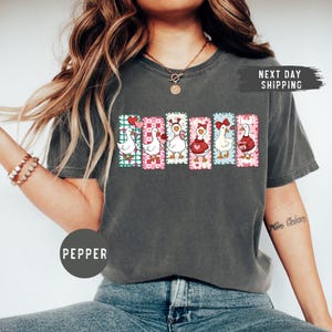Puede incluir: Camiseta gris oscuro con un gr&aacute;fico colorido de seis gansos de dibujos animados, cada uno con un dise&ntilde;o &uacute;nico, sobre fondos estampados. La palabra "PEPPER" est&aacute; impresa en la camiseta.