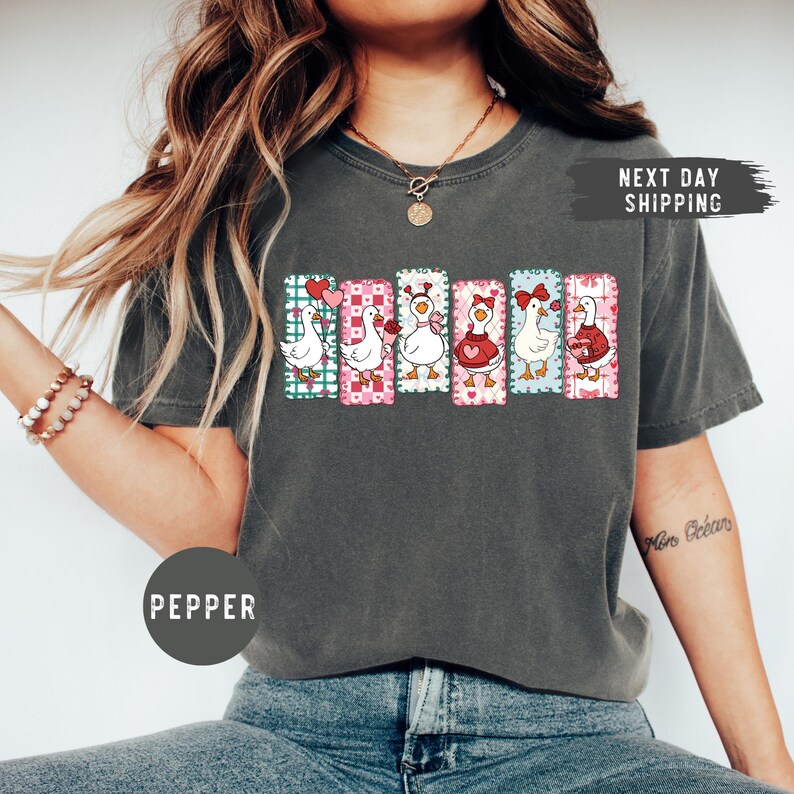 Puede incluir: Camiseta gris oscuro con un gr&aacute;fico colorido de seis gansos de dibujos animados, cada uno con un dise&ntilde;o &uacute;nico, sobre fondos estampados. La palabra "PEPPER" est&aacute; impresa en la camiseta.