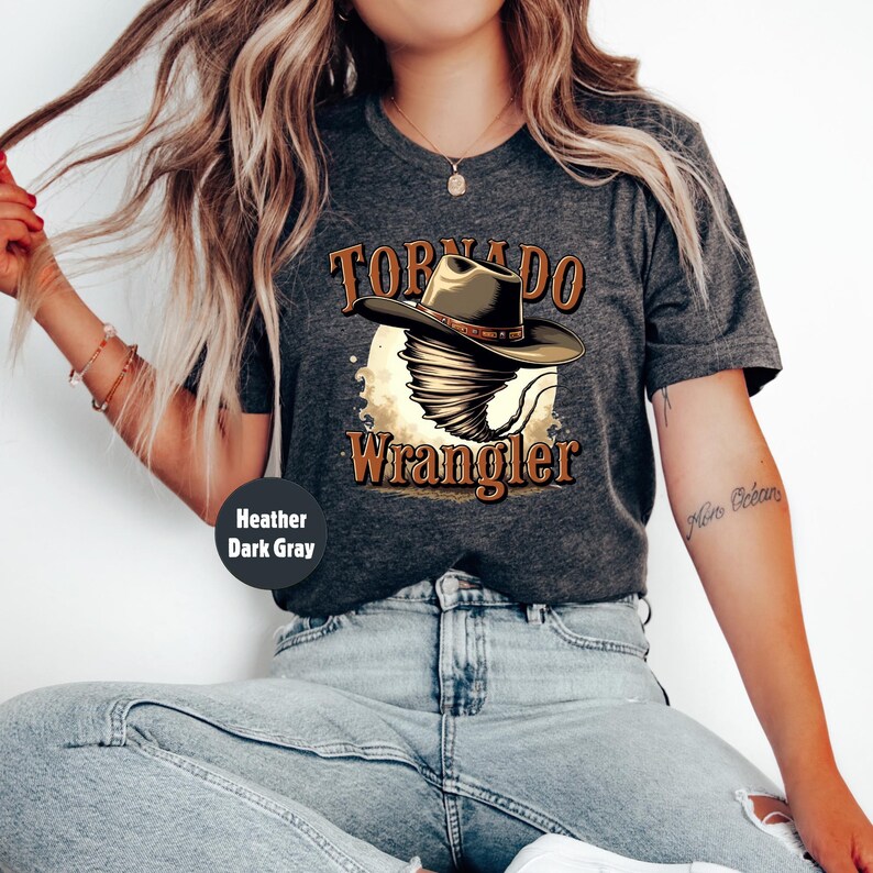 Op de afbeelding: Een donkergrijs heather t-shirt met een afbeelding van een tornado die een cowboyhoed draagt en de tekst "Tornado Wrangler".