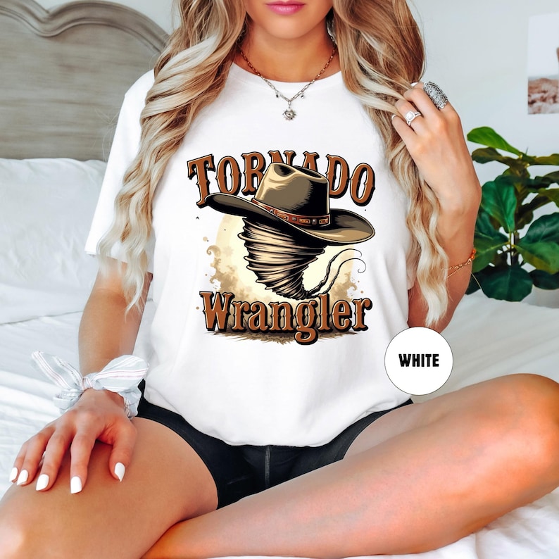 Op de afbeelding: Wit T-shirt met een afbeelding van een tornado die een cowboyhoed draagt en de tekst "Tornado Wrangler".