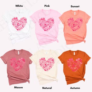 May include: Six short-sleeved t-shirts in white, pink, sunset, mauve, natural, and autumn colors. Each shirt features a heart design made of bows and the number 67 in pink.