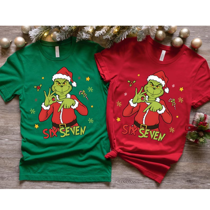 K&ouml;nnte beinhalten: Zwei kurz&auml;rmelige T-Shirts, eines gr&uuml;n und eines rot, mit einer Cartoon-Figur des Grinch mit Weihnachtsm&uuml;tze und rotem Anzug. Die Shirts zeigen den Text "SIX SEVEN" und weihnachtliche Grafiken.