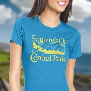 May include: A turquoise t-shirt with a yellow graphic that reads "Squirrels Of Central Park." The graphic features a squirrel illustration. The shirt has short sleeves and a crew neck.