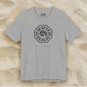 Heather grey short-sleeve t-shirt featuring the Dharma Initiative swan logo graphic from the TV show LOST in a vintage distressed style.