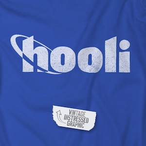 May include: A royal blue t-shirt featuring the word "Shooli" in a distressed white font with a curved design element. Below the word is a white graphic that reads "Vintage Distressed Graphic".
