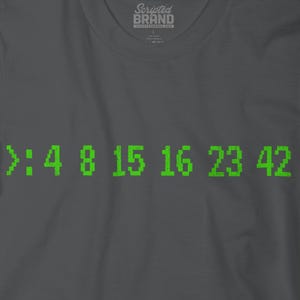 May include: Charcoal grey t-shirt featuring the green pixelated numbers >:4 8 15 16 23 42. The shirt has a crew neck and a brand logo at the top. The numbers are a reference to the TV show Lost.