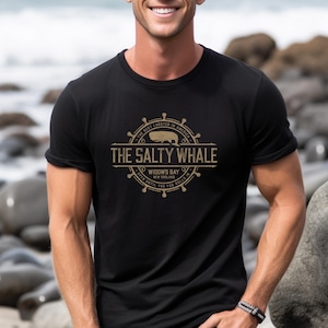 Man wearing black The Salty Whale vintage distressed pub logo t-shirt inspired by Widow's Bay Apple TV series, soft Bella+Canvas cotton tee