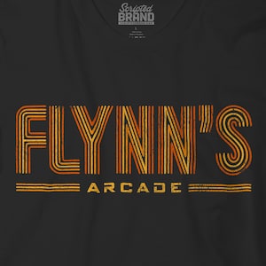 May include: Black t-shirt with the text "FLYNN'S ARCADE" in orange and yellow retro font. The shirt has a vintage, distressed look, with the brand logo at the top.