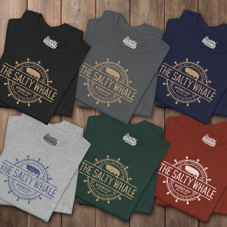 Six folded 'The Salty Whale' vintage distressed pub logo t-shirt inspired by Widow's Bay Apple TV series, soft Bella+Canvas cotton tee